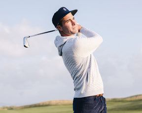 Man on golf course wearing The Wallace Hoodie Sweater: Heathered Gray, mid-swing with golf iron, showcasing its quilted design and streamlined fit.