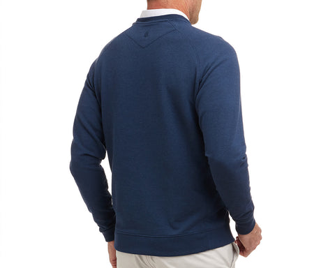 Man wearing The Kennedy Crewneck: Heathered Atlantic, a navy long-sleeve pullover over a white collared shirt, paired with light-colored pants from mid-back to below hips.