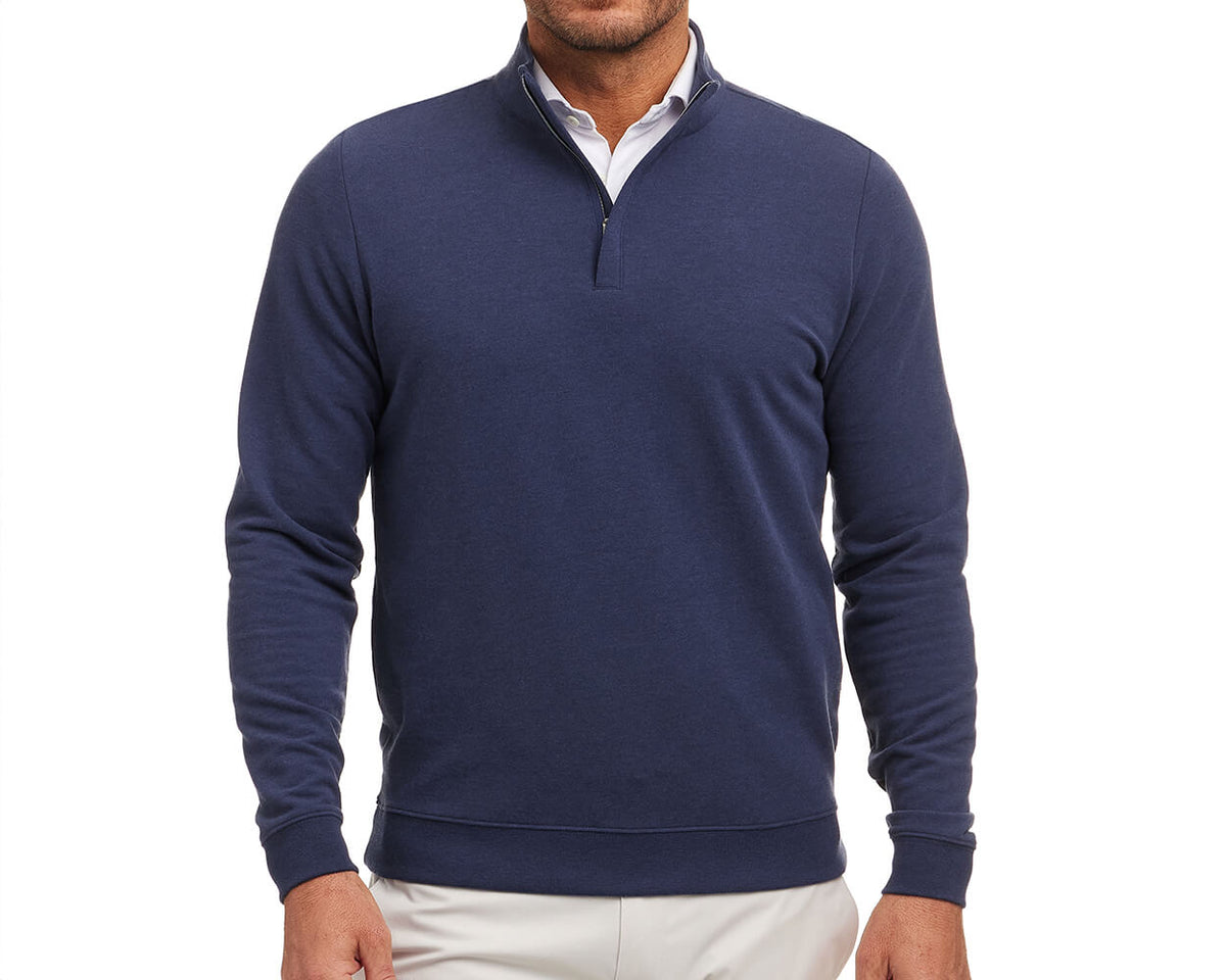 Man wearing The Harper Quarter-Zip: Heathered Atlantic, a navy pullover with a stand-up collar over a white shirt, paired with light-colored pants.