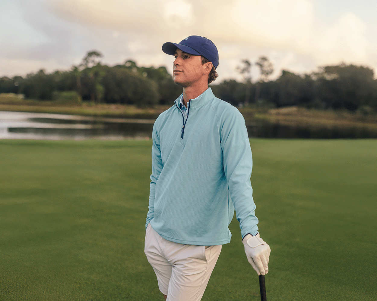 Man on golf course wearing The Stuart Quarter-Zip: Harbor, holding a golf club, showcasing its lightweight, textured rib fabric and superior softness.