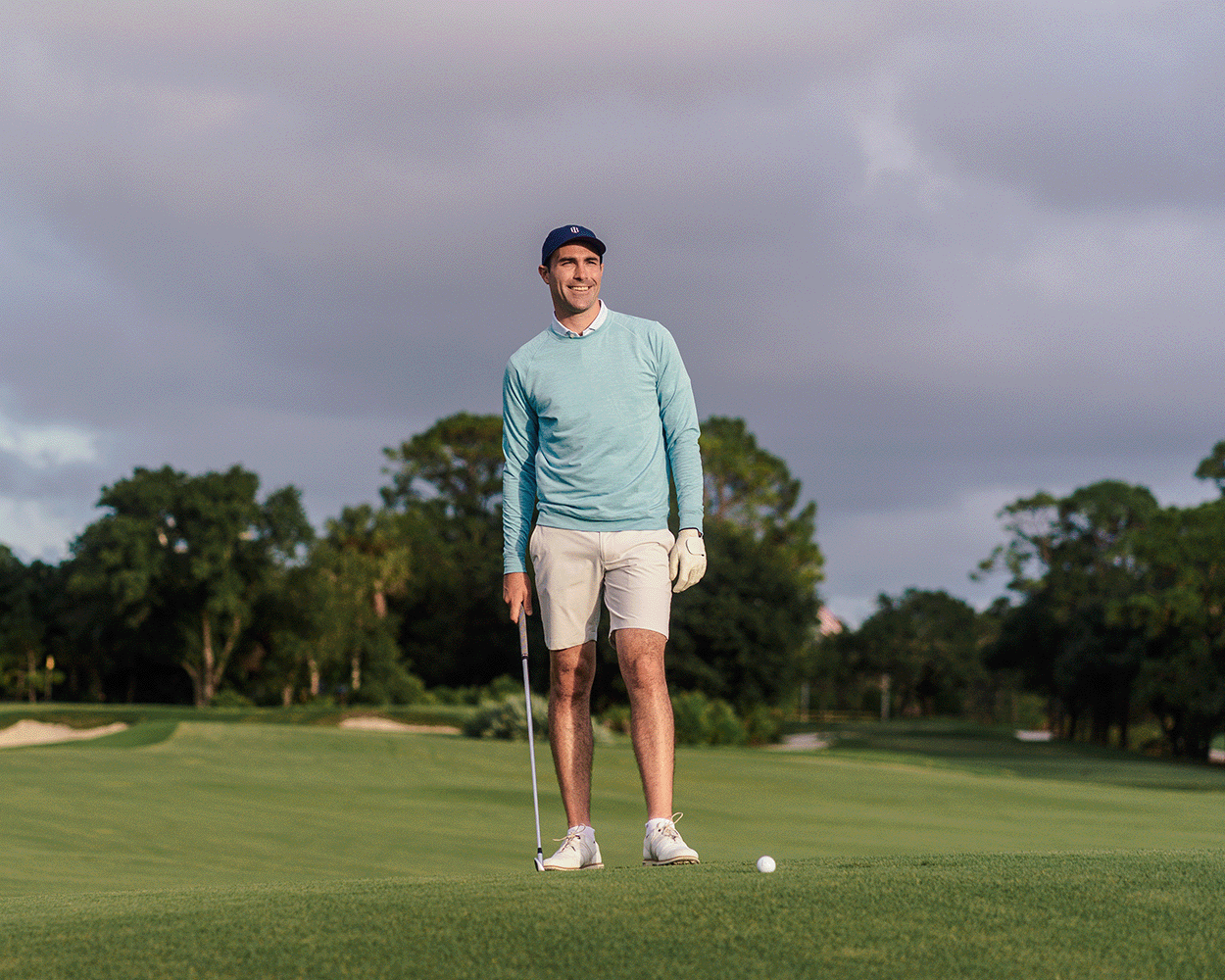 Man on golf course wearing The Laidlay Crewneck: Heathered Harbor, lining up a putt, showcasing its heathered texture and signature fit for mobility.