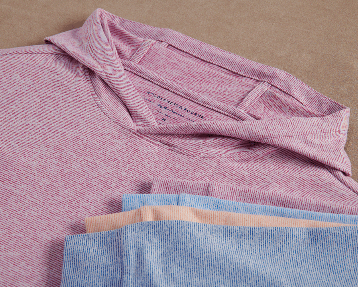The Hamilton Hoodie: Heathered Cabernet & White features a subtle heathered stripe, lightweight performance blend, and visible Holderness & Bourne label on the folded pink-and-white shirt.
