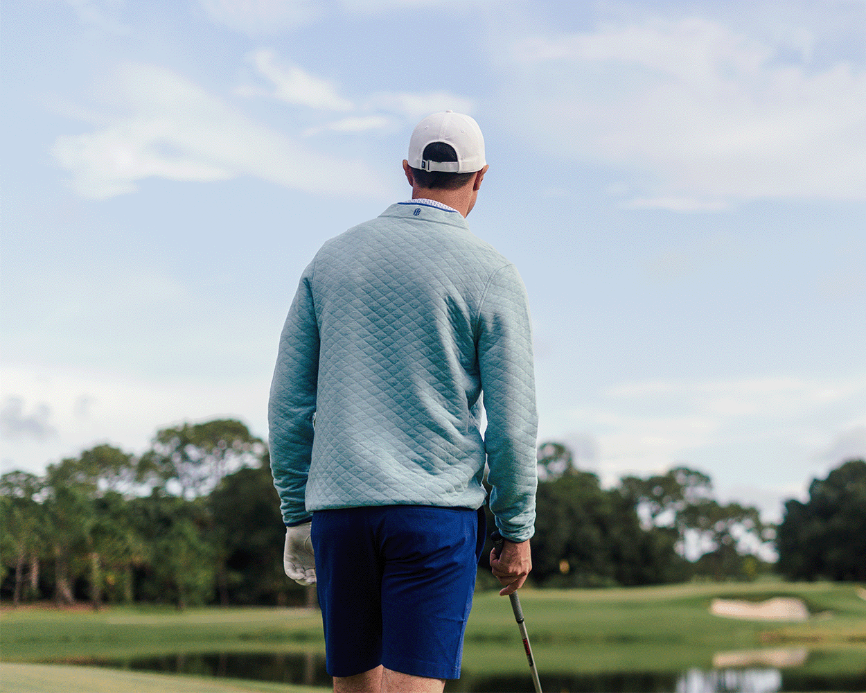 Person wearing The Sullivan Quarter-Snap: Heathered Harbor on a golf course, holding a club, showcasing its quilted design and casual, versatile style.