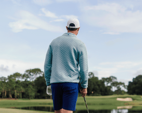 Person wearing The Sullivan Quarter-Snap: Heathered Harbor on a golf course, holding a club, showcasing its quilted design and casual, versatile style.