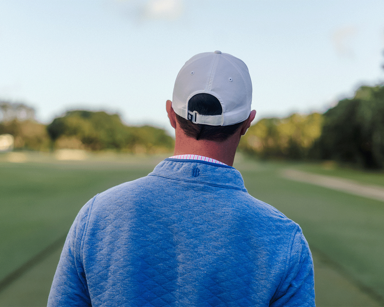 Person in a backward cap and light blue Sullivan Quarter-Snap pullover on a golf course, showcasing its quilted insulation and casual style.