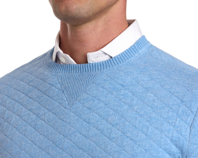 Person wearing The Ward Crewneck Sweater in Heathered Vista Blue, showcasing its diamond jacquard knit over a white collared shirt, highlighting its texture and layering style.