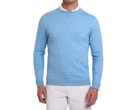 Man wearing The Ward Crewneck Sweater: Heathered Vista Blue, showcasing a diamond-quilted pattern over a white collared shirt, paired with light trousers.