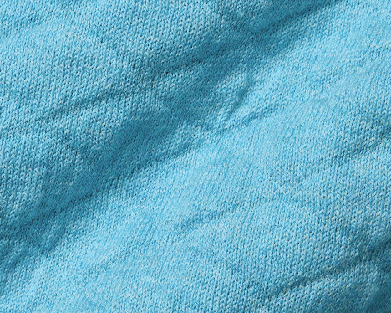 Close-up of The Wallace Hoodie Sweater: Heathered Harbor, showcasing the intricate light-blue knit texture and ribbed side panels in 100% Egyptian cotton.