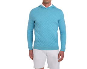 The Wallace Hoodie Sweater: Heathered Harbor, shows a light-blue diamond-quilted pullover with a hood over a white collared shirt, paired with light shorts.