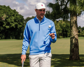 Man on golf course wearing The Rodgers Quarter-Zip: Horizon Blue, holding a golf club, showcasing its stretchy, midweight design ideal for golf or casual wear.