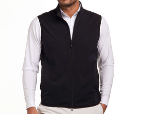 Man wearing The Ventura Vest: Black, a sleeveless zip-front vest, over a white shirt. Features perforated fabric and zippered pockets for functionality.