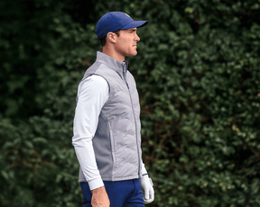 Man wearing The Benton Vest: Gray, featuring a quilted front and knit back for mobility, with a two-way zipper, holding a golf glove.