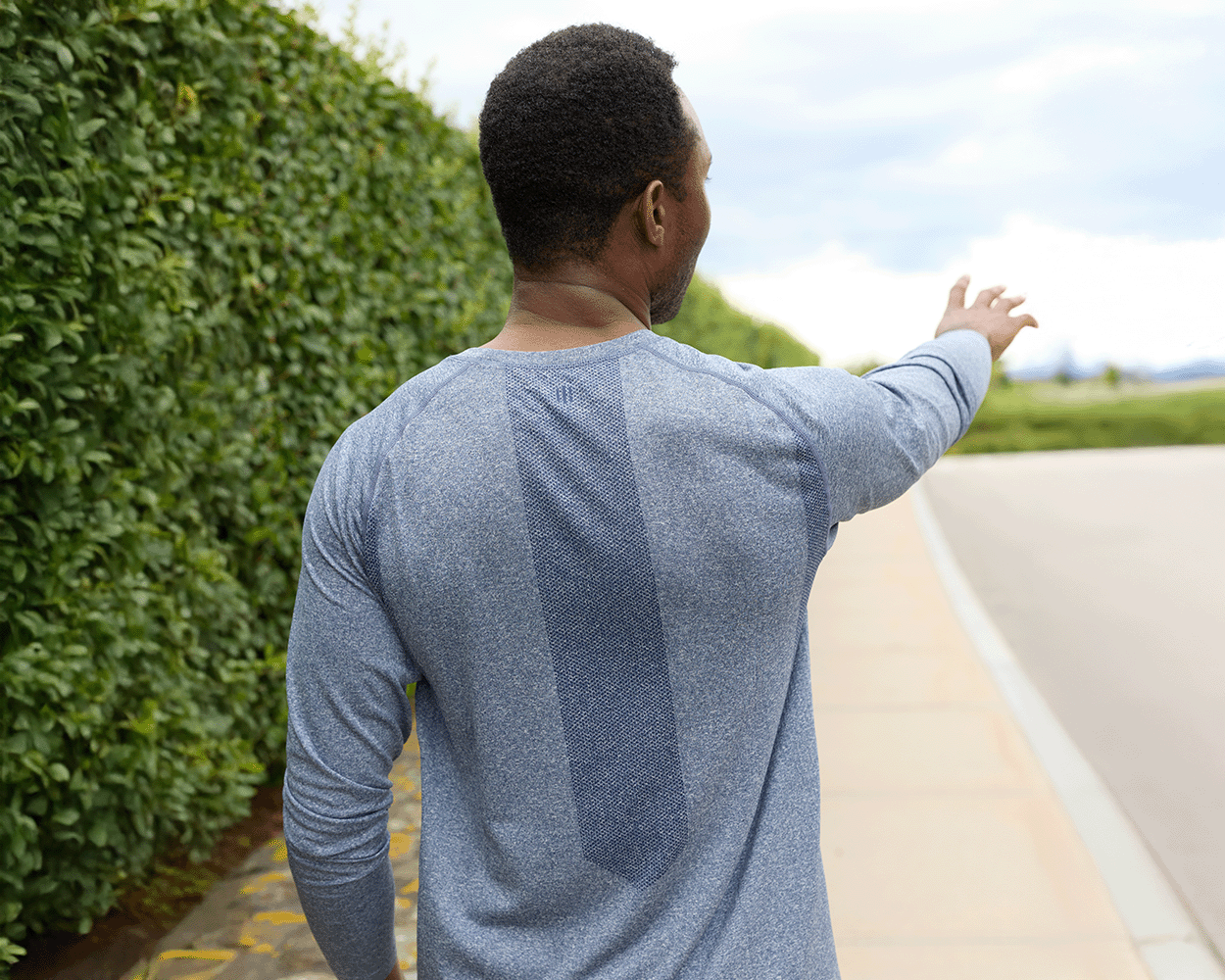 Person in heathered navy long-sleeve athletic shirt, The Carr T-Shirt, stands on sidewalk, arm outstretched, showcasing its sleek fit and versatile design.