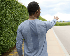 Person in heathered navy long-sleeve athletic shirt, The Carr T-Shirt, stands on sidewalk, arm outstretched, showcasing its sleek fit and versatile design.