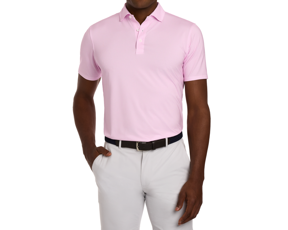 The Hanover Shirt: Belmont, a light-pink polo with geometric pattern, features a structured collar and four-way stretch, worn with grey trousers and a woven belt.