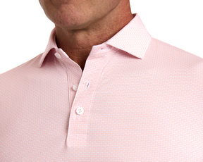 Close-up of The Hanover Shirt: Nectarine, showcasing a light pink geometric pattern on a collared performance jersey with white buttons, emphasizing its structured spread collar.