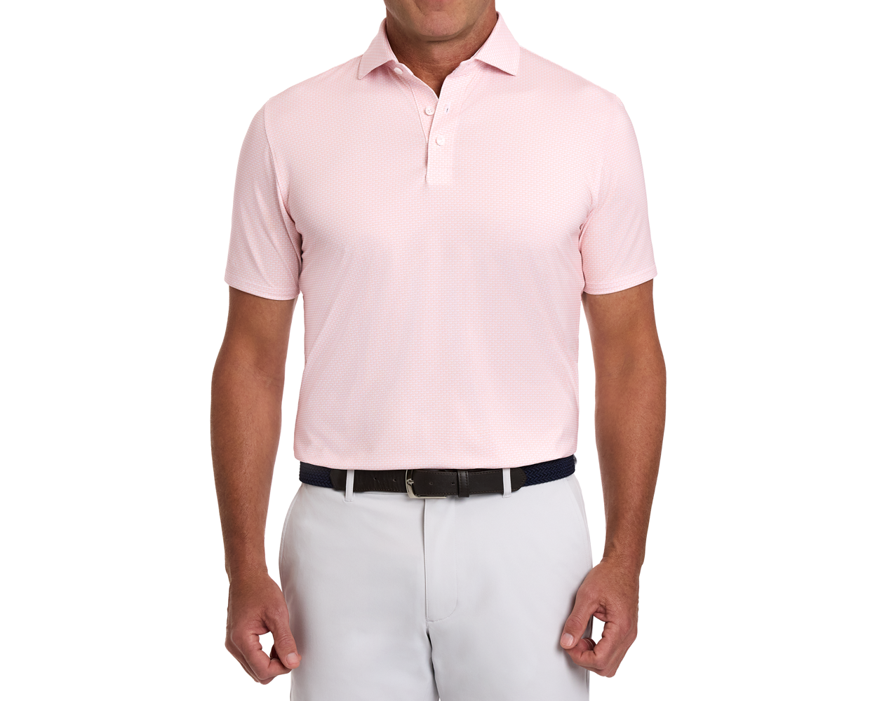 The Hanover Shirt: Nectarine, a short-sleeve polo with geometric jet pattern, tucked into light-gray trousers, featuring a dark woven belt.