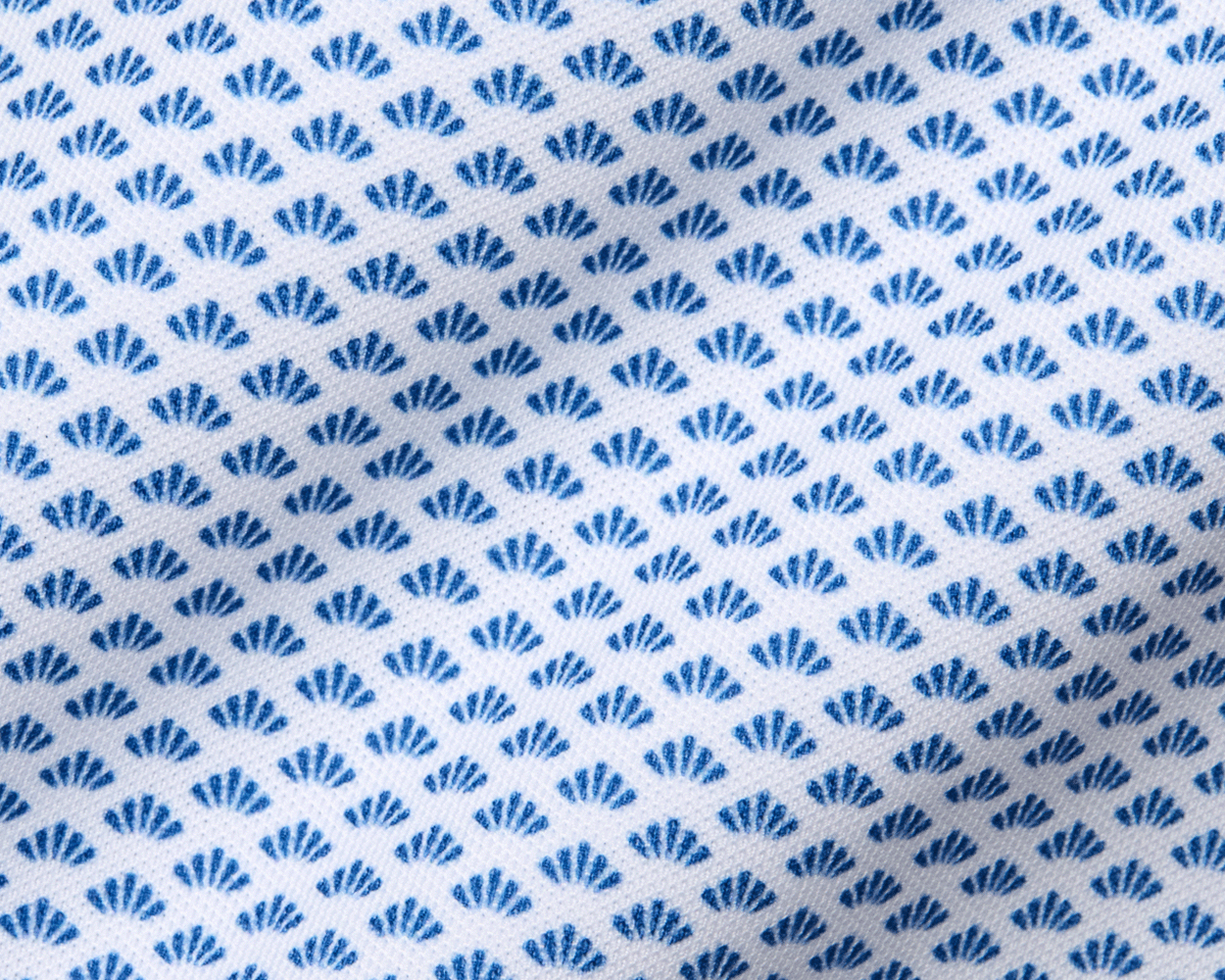 The Geiger Shirt: Maidstone Blue features a close-up of its white fabric with a grid of small blue fan motifs, highlighting its breathable, moisture-wicking pique texture.