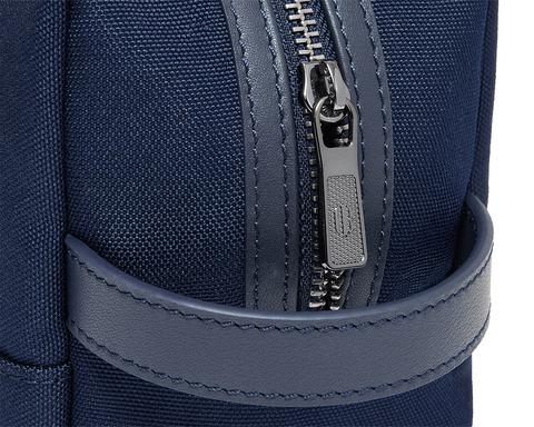 The Littler Dopp Kit features a navy-blue fabric with leather-trimmed strap, metal zipper, and water-resistant interior, ideal for travel and personalization.