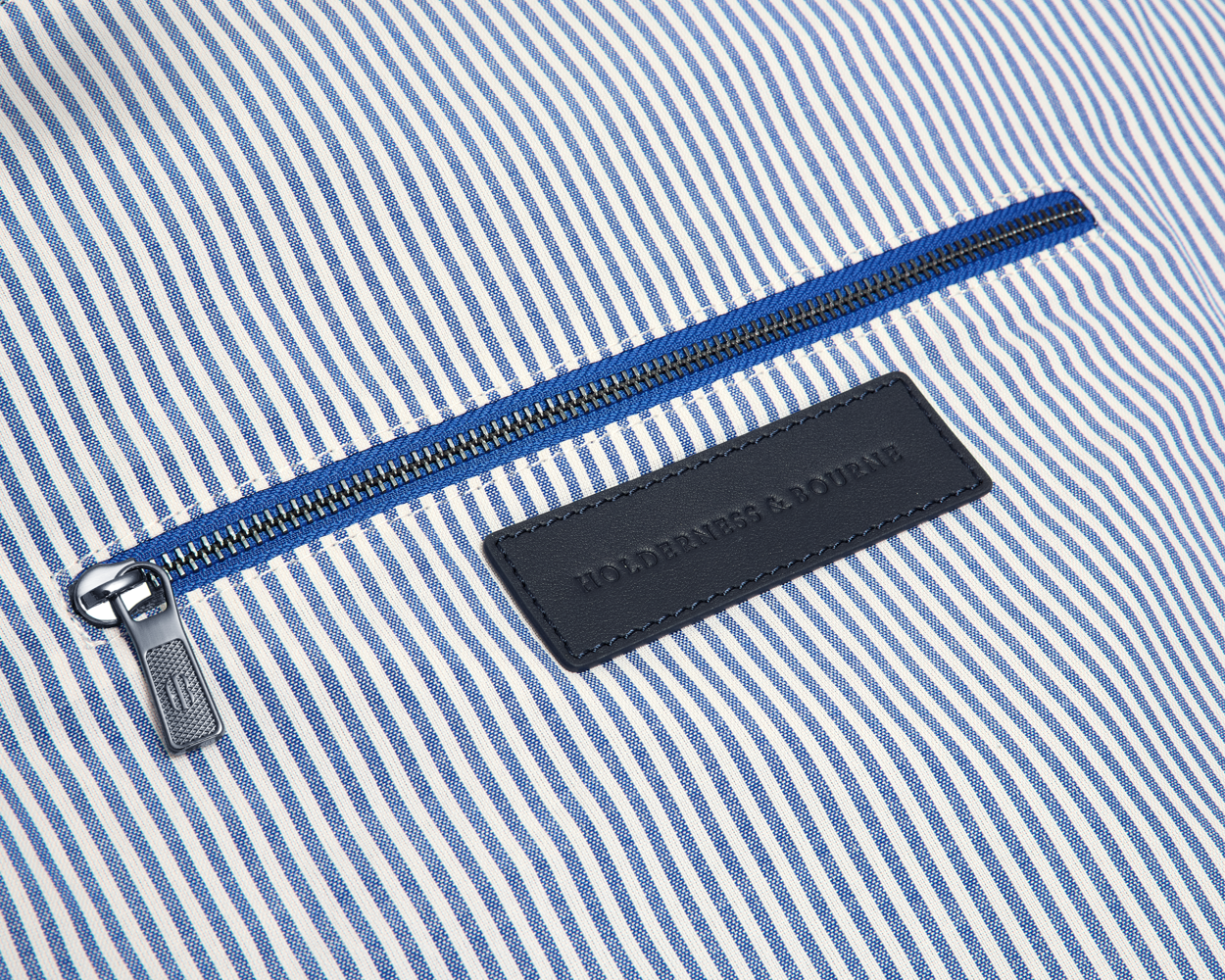 The Byers Duffel Bag: Navy Ballistic, featuring blue-and-white pinstripe interior, metal zipper, and embossed leather brand patch, showcasing its sleek interior zip pocket.
