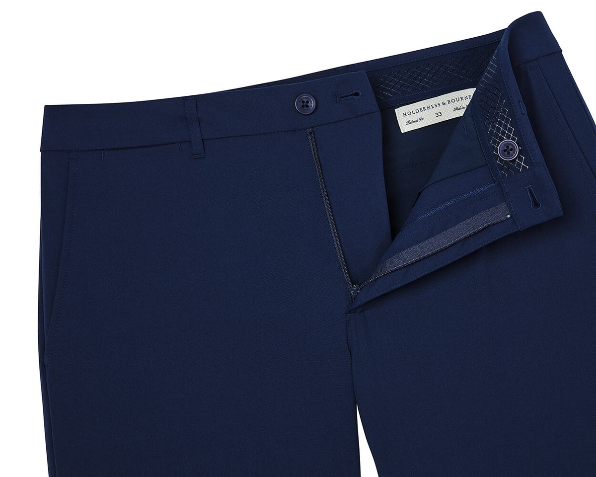 The Harwood Short: Navy men's trousers, laid flat, with open waistband showing Holderness & Bourne, 33 label, emphasizing comfort and golfer-friendly features.