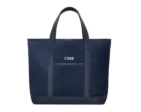 The Treadwell Tote: Navy Ballistic with white CMB monogram, features leather-trimmed handles, front pocket, and an open-top design for versatile use.
