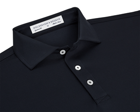 The Anderson Shirt: Black, featuring a dark-navy polo with a classic point collar, three white buttons, and a woven label, offering stretch and moisture-wicking comfort.