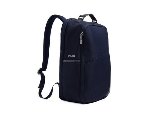 The Broughton Backpack: Navy Ballistic - Slate Blue Embroidery, featuring a sleek design with zippered compartments, padded straps, and personalized initials CMB on the front.