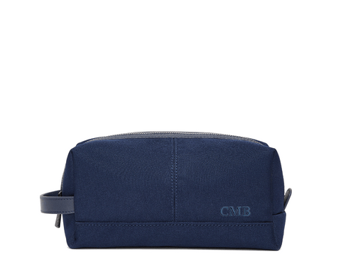 The Littler Dopp Kit: Navy Ballistic - Navy Embroidery, a sleek navy travel toiletry bag with a leather handle, top zipper, and debossed CMB initials.