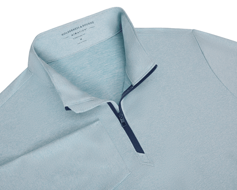 The Bell Quarter-Zip: Heathered Harbor features a teal-toned, textured knit with a navy zipper. It's lightweight, breathable, and designed with a modern drop-tail silhouette.