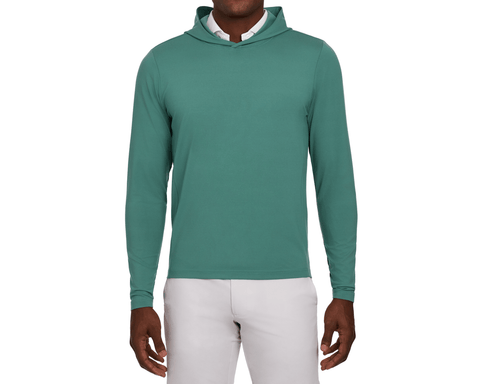Model wearing The Jackson Hoodie: California Spruce, showing its hood, long sleeves, and plain front, with a white collar and light gray pants.