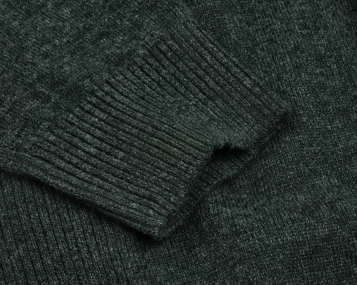 The Logan Hoodie Sweater: Heathered Ivy, showcasing a close-up of the ribbed sleeve cuff and textured knit fabric in a luxurious Merino wool and cashmere blend.