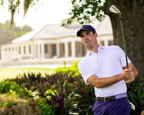 Man on golf course wearing The Macdonald Shirt: White, a collared polo offering breathable comfort and modern style, mid-swing with iron club.