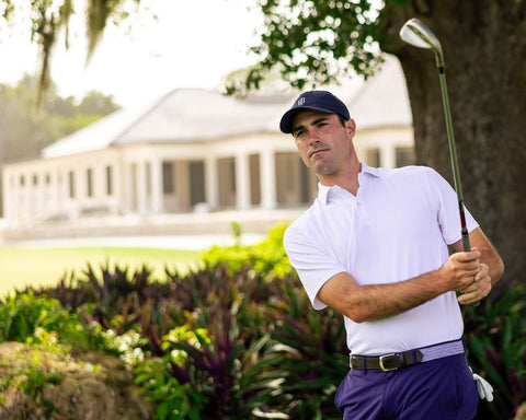 Man on golf course wearing The Macdonald Shirt: White, a collared polo offering breathable comfort and modern style, mid-swing with iron club.