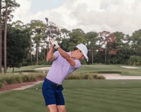 Golfer wearing The Maxwell Shirt: Tudor & White, mid-swing on a fairway, showcasing its modern striped design and comfortable, performance-focused material.