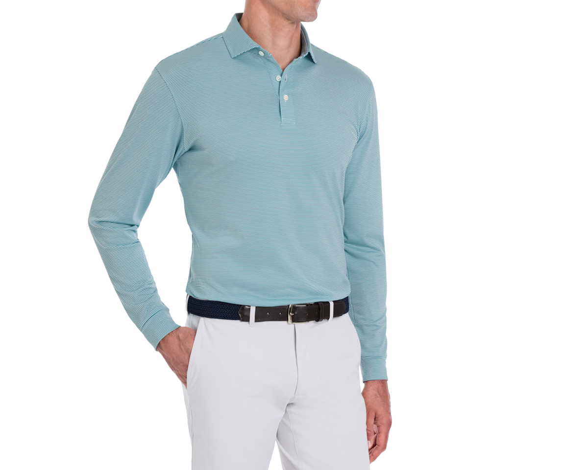 Man wearing The Burke Shirt: Harbor & White, a striped long-sleeve polo with UPF 50+, tucked into light pants with a woven belt.
