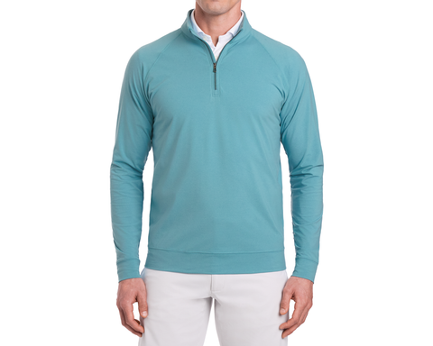 Man wearing The Westland Quarter-Zip: Heathered Harbor, a light teal-blue pullover with gunmetal chrome trim, over a white shirt and beige pants.