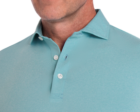 Man wearing The Holland Shirt: Heathered Harbor, showcasing a light aqua polo with a structured spread collar, white buttons, and subtle stripe detailing.
