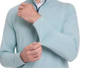 Person wearing The Bell Quarter-Zip: Heathered Harbor, adjusting a sleeve cuff of the light teal pullover, showcasing its modern drop-tail silhouette and signature fit.