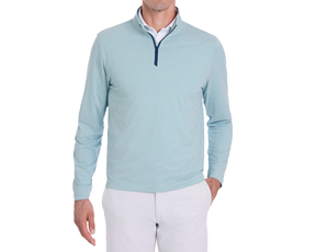 Model wearing The Bell Quarter-Zip: Heathered Harbor, showcasing its modern drop-tail silhouette over a white shirt, paired with light trousers, right hand in pocket.