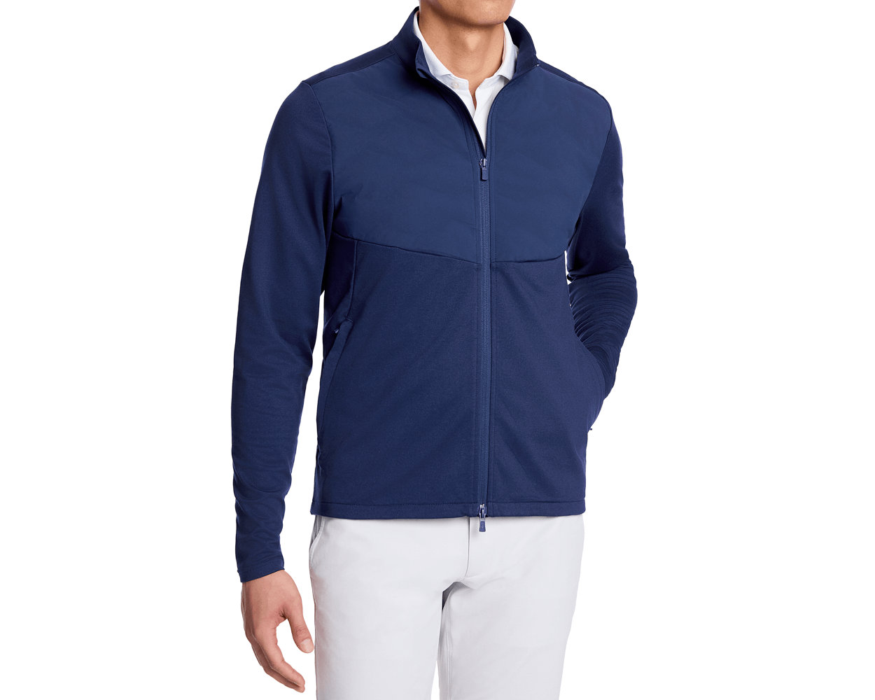The Brodie Jacket: Navy, featuring a stand-up collar, zip pockets, and insulated panels, layered over a white polo, paired with light-colored pants.