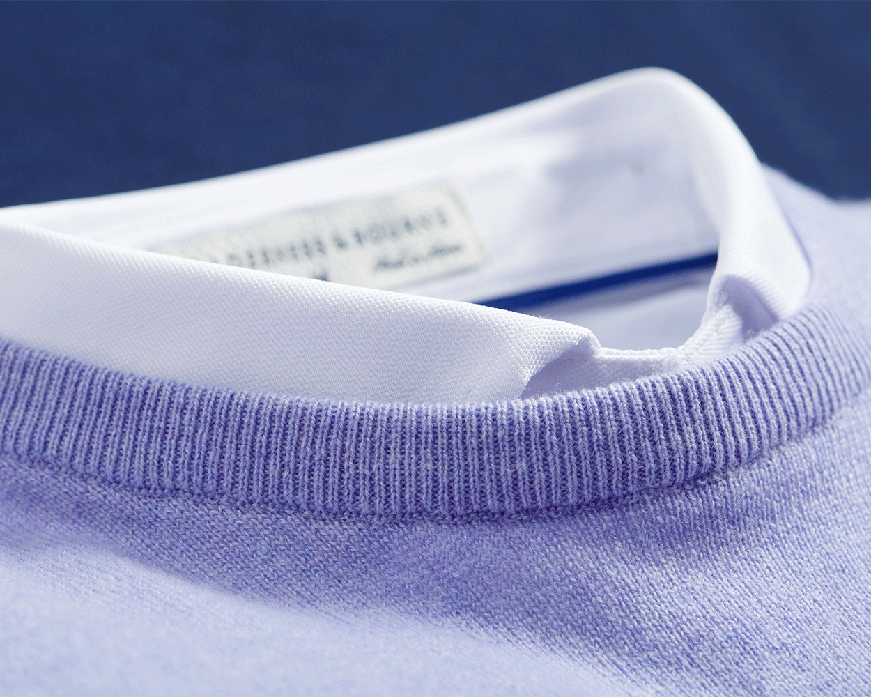 The Buckley Crewneck Sweater: Heathered Lavender, showcasing a close-up of its knit texture and classic crew neck layered over a white shirt collar.