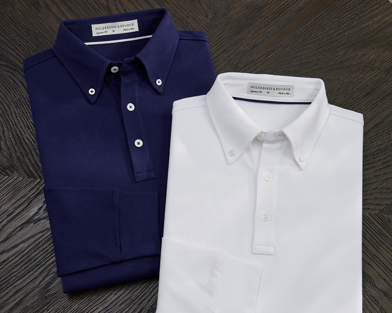 The Burton Shirt: White, a long-sleeve polo with a button-down collar, three buttons, and stretch ribbed cuffs, displayed alongside its navy counterpart on a wooden surface.