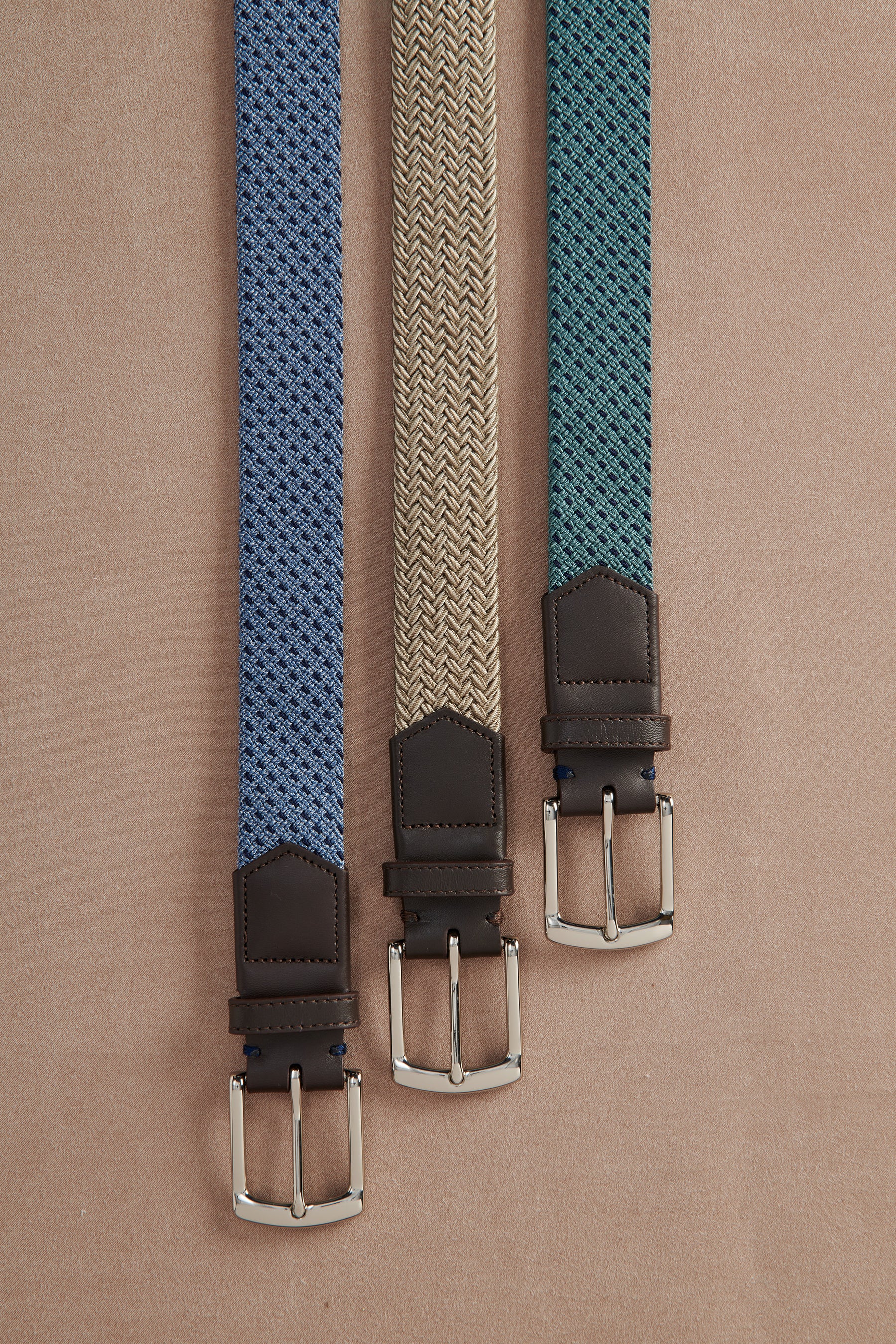 Three belts with different patterns and colors on a beige background