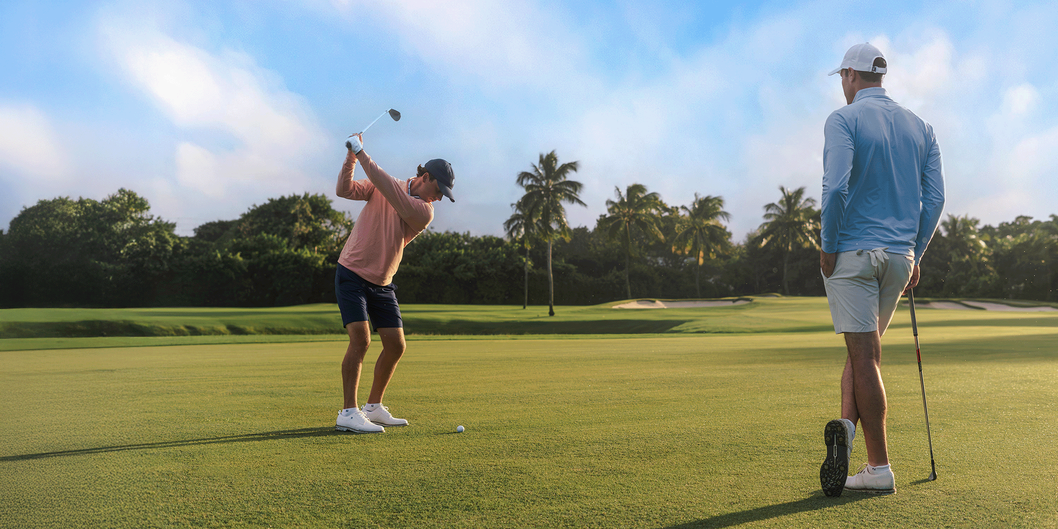 Two golfers on a green course with trees in the background