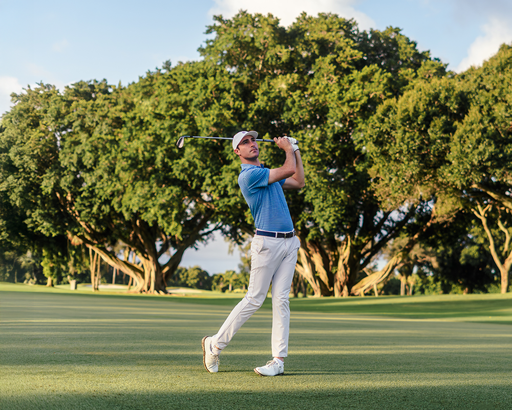Man playing golf on a green course with trees in the background