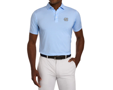 Model wearing University of North Carolina Norman Shirt: Vista Blue & Horizon Blue, featuring a light blue geometric print, the NC logo on the left chest, a dark belt, and white pants.