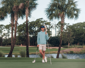 The Wallace Hoodie Sweater: Heathered Harbor on a golfer, featuring a quilted design, ribbed panels, and a relaxed fit, perfect for cool weather.