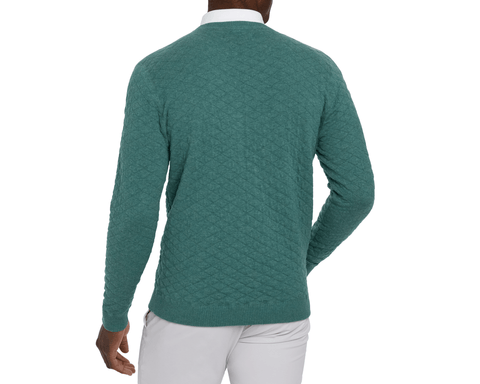 Back view of a male model wearing The Ward Crewneck Sweater: Heathered California Spruce, showing the diamond jacquard knit, ribbed hem, and light gray pants.