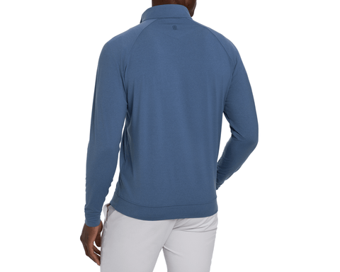 Back view of a model wearing The Westland Quarter-Zip: Heathered Pacific Blue, showing raglan sleeves, ribbed hem, and a small upper-back logo with light gray pants.